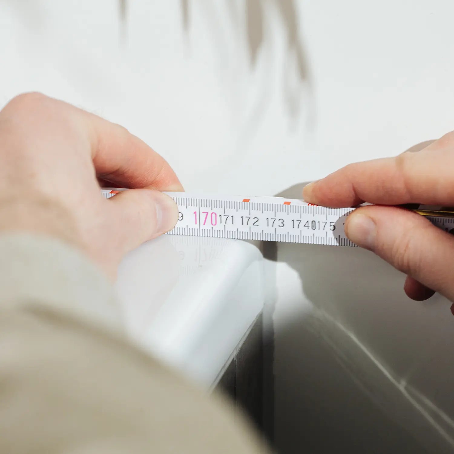 Eine Person misst sorgfältig den Rand einer Badewanne mit einem Maßband, um eine präzise Passform für eine maßgeschneiderte Badewannenabdeckung bzw. Abdeckung Badewanne zu gewährleisten. Das genaue Messen ist ein entscheidender Schritt, um sicherzustellen, dass die Abdeckung perfekt sitzt und optimalen Schutz sowie eine ästhetische Ergänzung für das Badezimmer bietet.