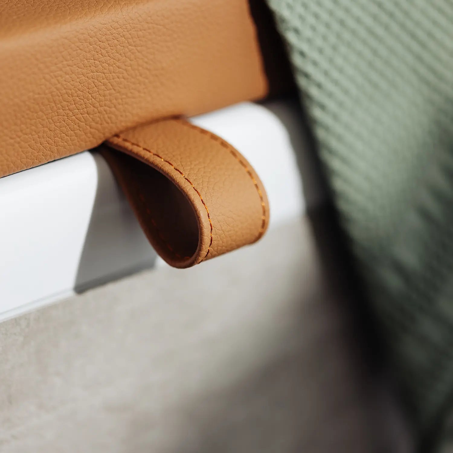 Eine Nahaufnahme einer Badewannenabdeckung bzw. Abdeckung Badewanne in warmem Cognac-Braun zeigt eine detaillierte Ansicht der hochwertigen Lederschlaufe, die für einfaches Anheben und Handhabung sorgt. Neben der Abdeckung liegt ein grünes Handtuch, das die sorgfältige Verarbeitung und die durchdachte Funktionalität des Designs betont.