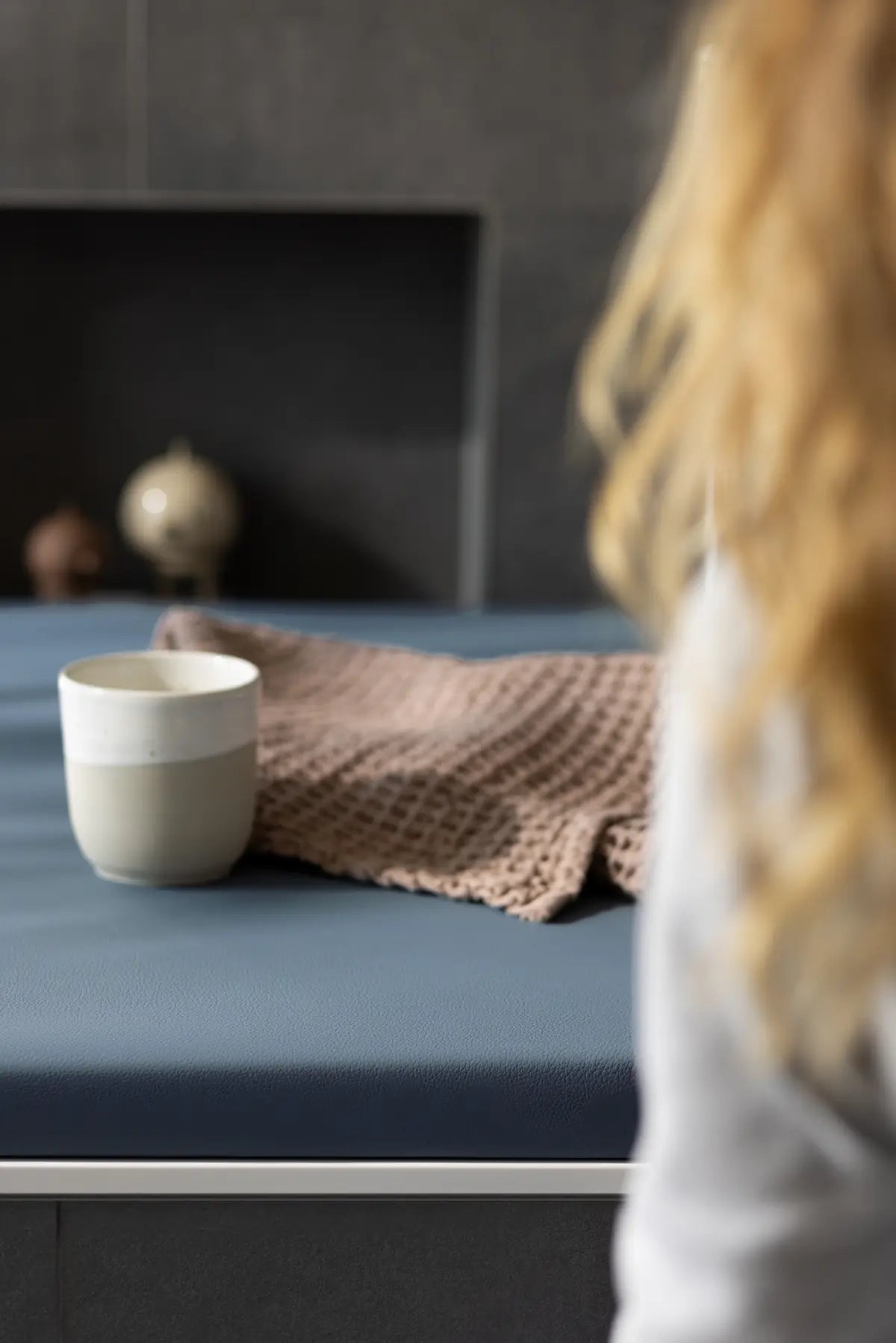 Elegante Badewannenabdeckung bzw. Abdeckung Badewanne in dunklem Blau, die als Sitz- und Ablagefläche dient. Auf der Abdeckung liegen eine Keramiktasse und ein weiches Handtuch, was eine gemütliche Atmosphäre in einem modernen Badezimmer mit dunklen Akzenten vermittelt.