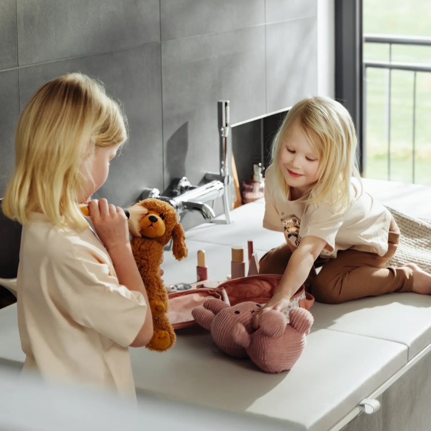 Zwei Kinder spielen auf einer cremeweißen Matti-Badewannenabdeckung von hejdeck mit Kuscheltieren und Spielzeug. Die Abdeckung verwandelt die Badewanne in eine sichere Spielfläche und zeigt, wie vielseitig nutzbar der zusätzliche Stauraum und die robuste Oberfläche im Alltag sind.